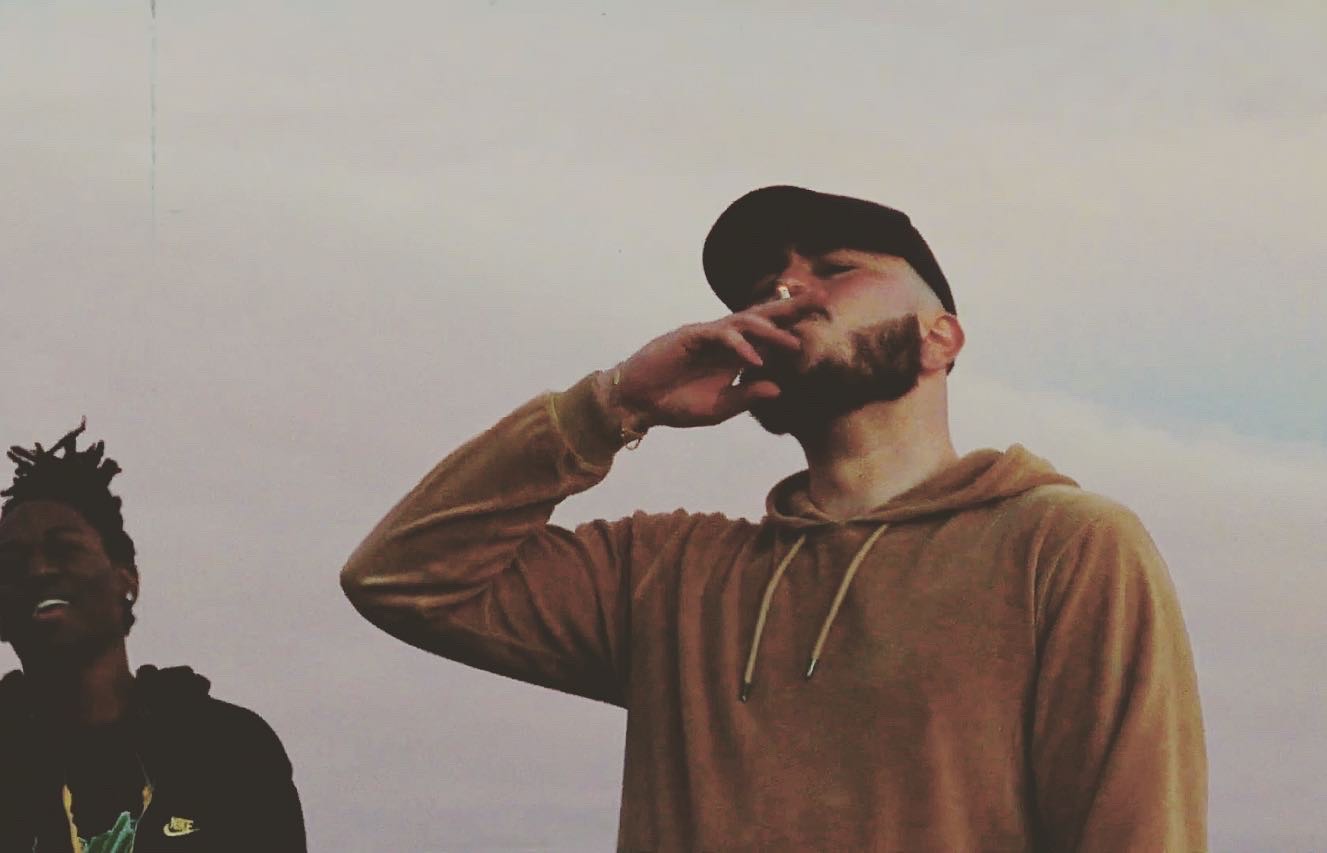 two men standing next to each other smoking a cigarette